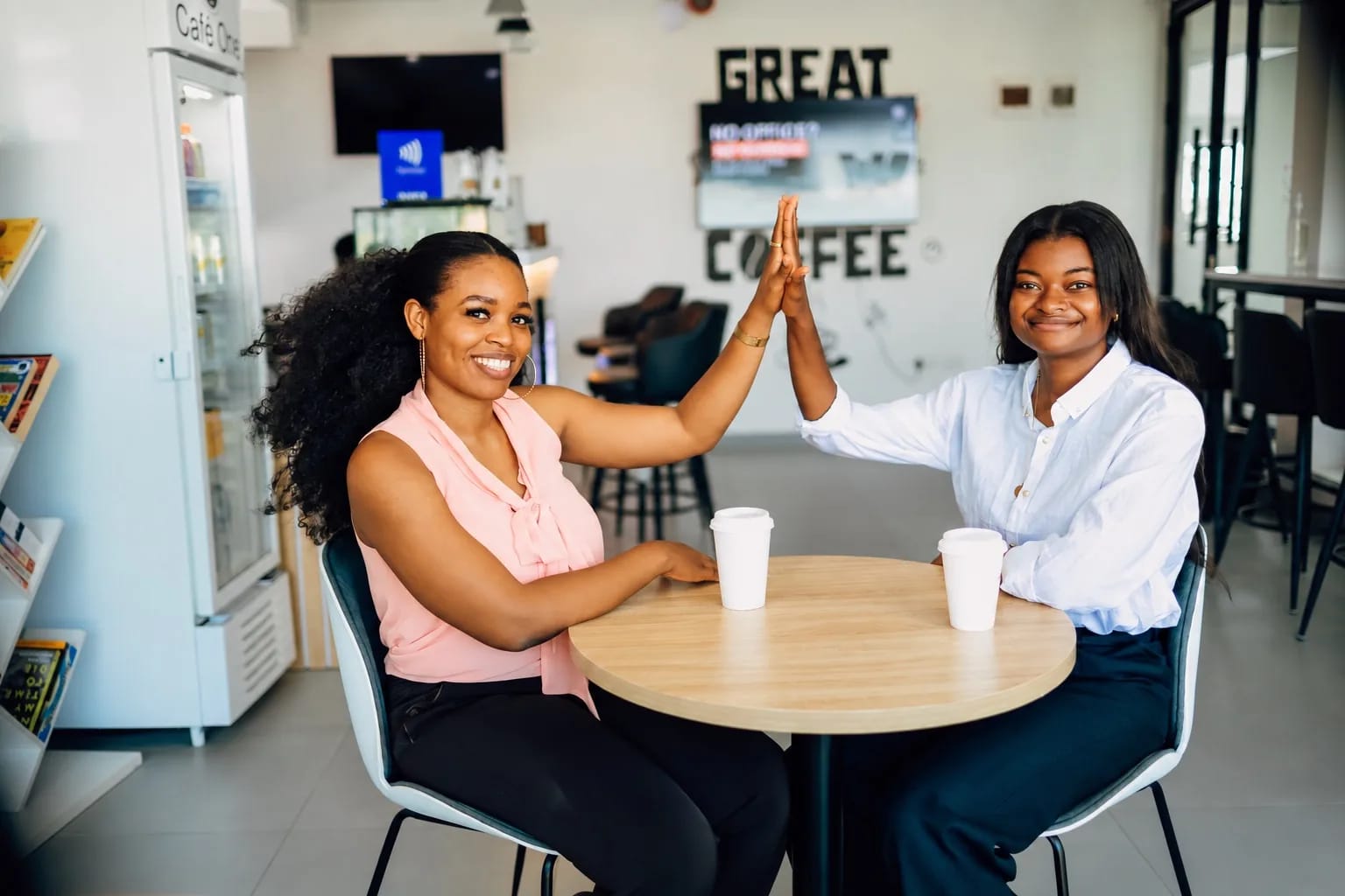 Two colleagues celebrating with a high-five at a cafe table