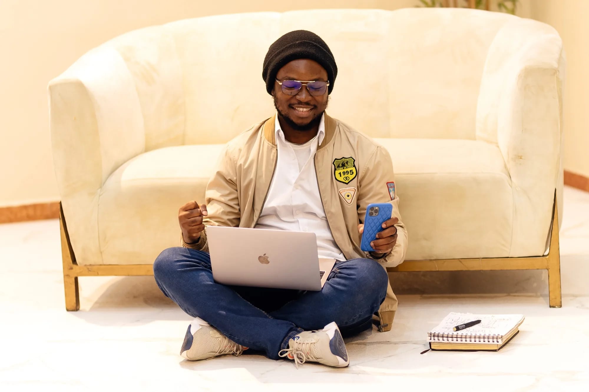 Man sitting beside a sofa with a laptop and phone